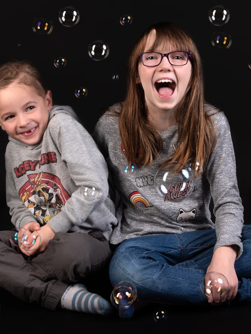Zwei Geschwister spielen beim Fotoshooting mit Seifenblasen