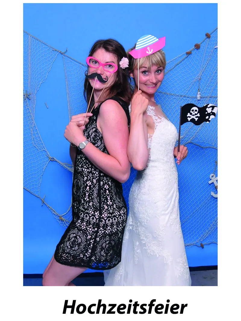 Zwei Gäste posieren mit Requisiten vor der Fotobox auf einer Hochzeit