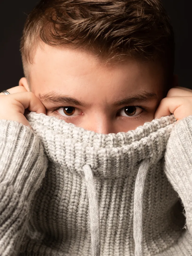 Portrait eines jungen Mannes mit Pullover vor dunklem Hintergrund
